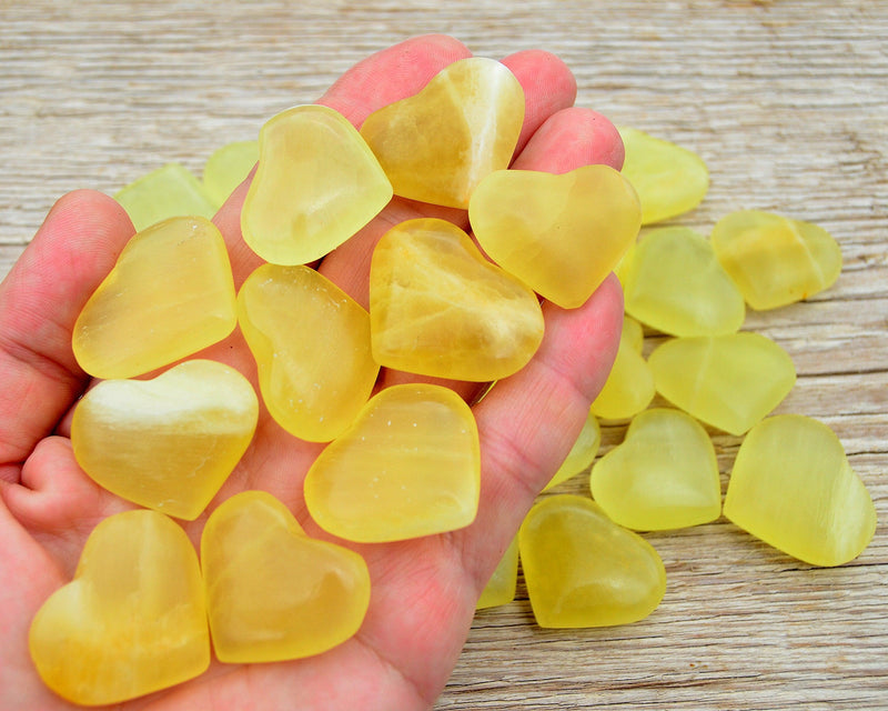 Ten lemon calcite crystal hearts 25mm-30mm on hand with background with some hearts on wood table
