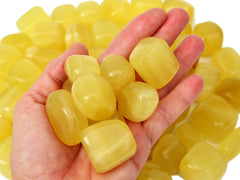 Some lemon calcite cube tumbled crystals on hand with background with some stones on white