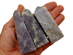 Three purple lepidolite crystal obelisks 90mm on hand with white background