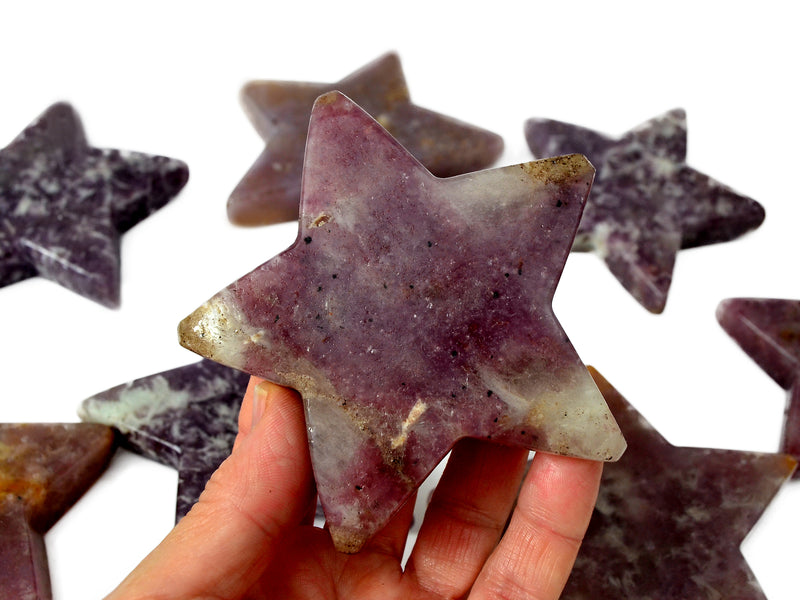 One purple lepidolite star crystal on hand with background with some stars on white