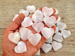 Ten  pink mangano calcite crystal hearts 30mm-35mm on hand with background with some hearts on wood table