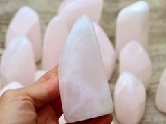 One pink mangano calcite free form 90mm on hand with background with some specimens on wood table