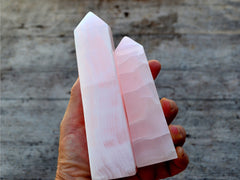 Two pink mangano calcite crystal obelisks 90mm-150mm on hand with wood background