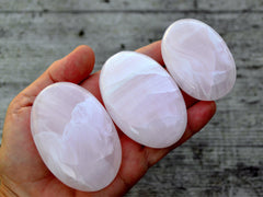 Three pink mangano calcite palm stones 55mm-90mm on hand with wood background