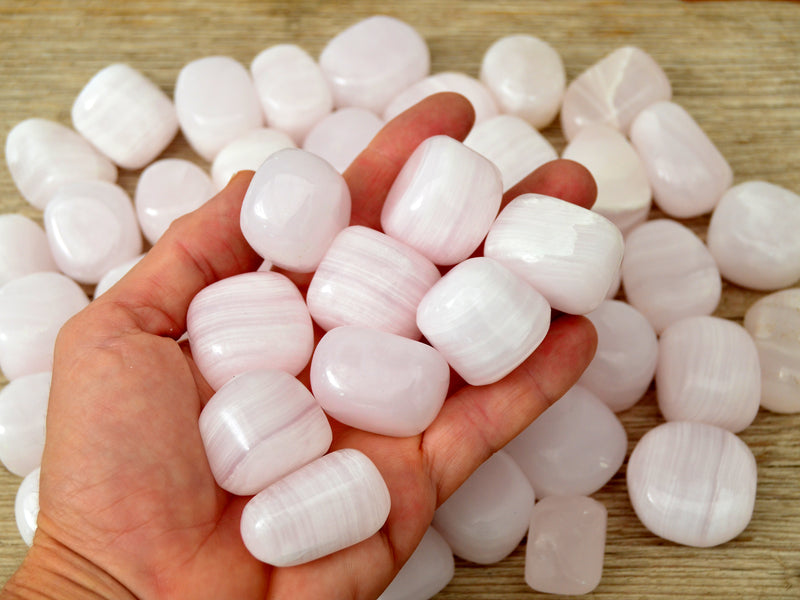 Pink mangano calcite tumbled stones on hand with background with some crystals on wood table