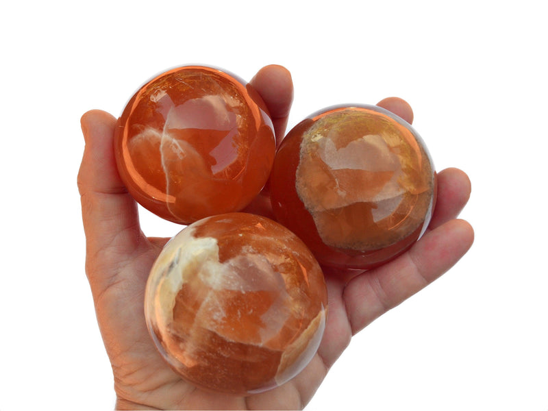 Three honey calcite spheres 60mm-70mm on hand with white background