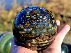 Large brown ocean jasper crystal sphere 100mm on hand with nature background