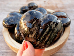 Large ocean jasper crystal heart 70mm on hand with background with some hearts inside a wood bowl