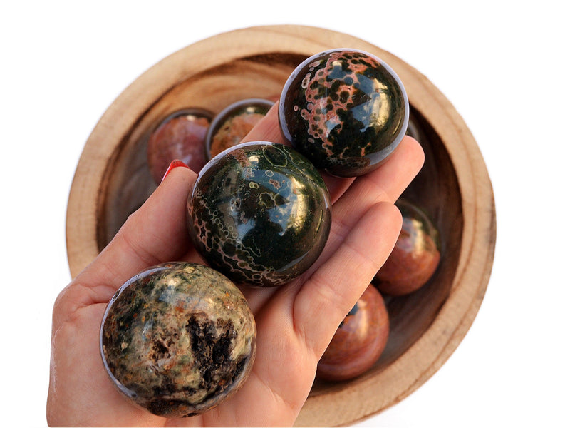 Three ocean jasper crystal spheres 45mm-55mm on hand with background with some crystals inside a wood bowl