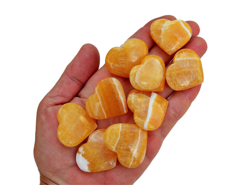 Ten small orange calcite heart shapped minerals on hand with white background