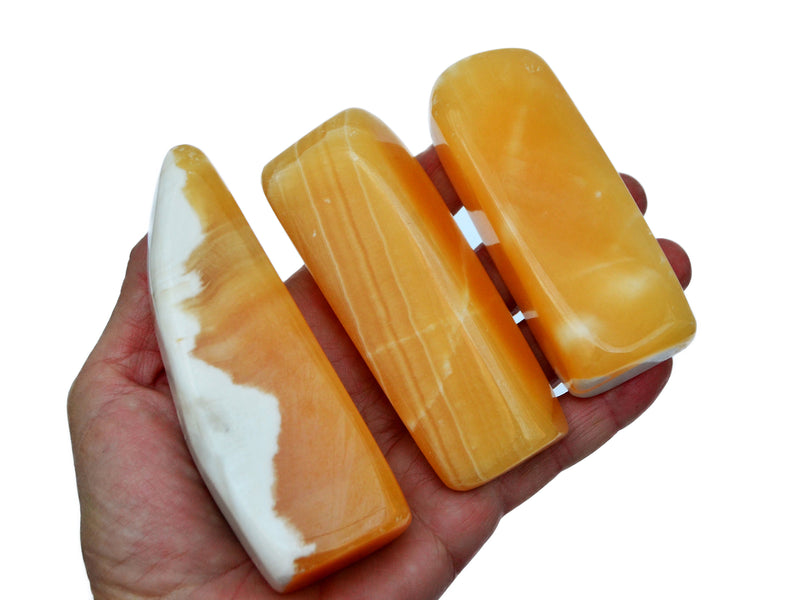 Three orange calcite free forms 80mm on hand with white background