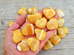 Ten orange calcite crystal hearts 30mm-35mm on hand with background with some hearts on wood table
