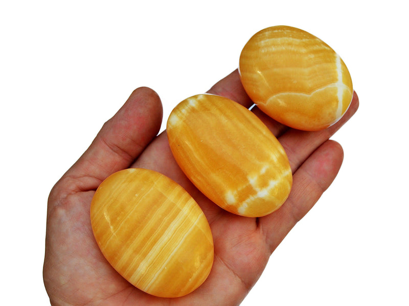 Three orange calcite palm stones 50mm-70mm on hand with white background
