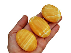 Three orange calcite palm stones 50mm-70mm on hand with white background