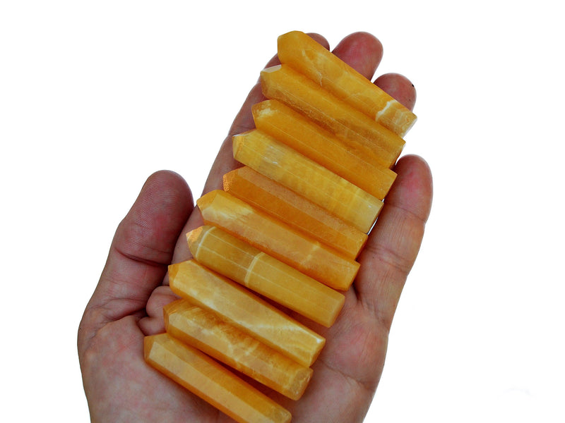 Ten mini orange calcite crystal points on hand with white background
