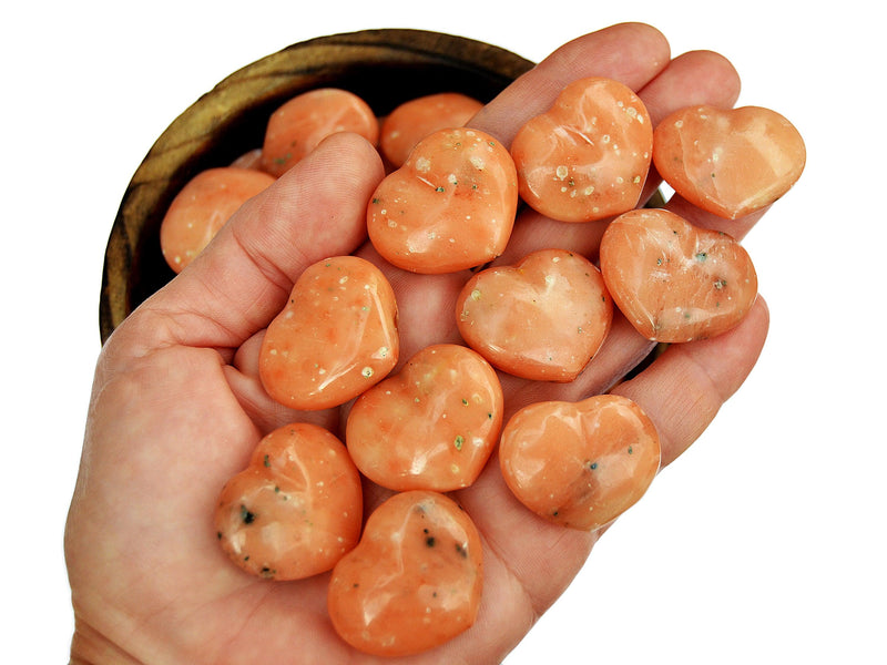 Some orange calcite heart crystals 30mm on hand with background with some stones inside a wood bowl