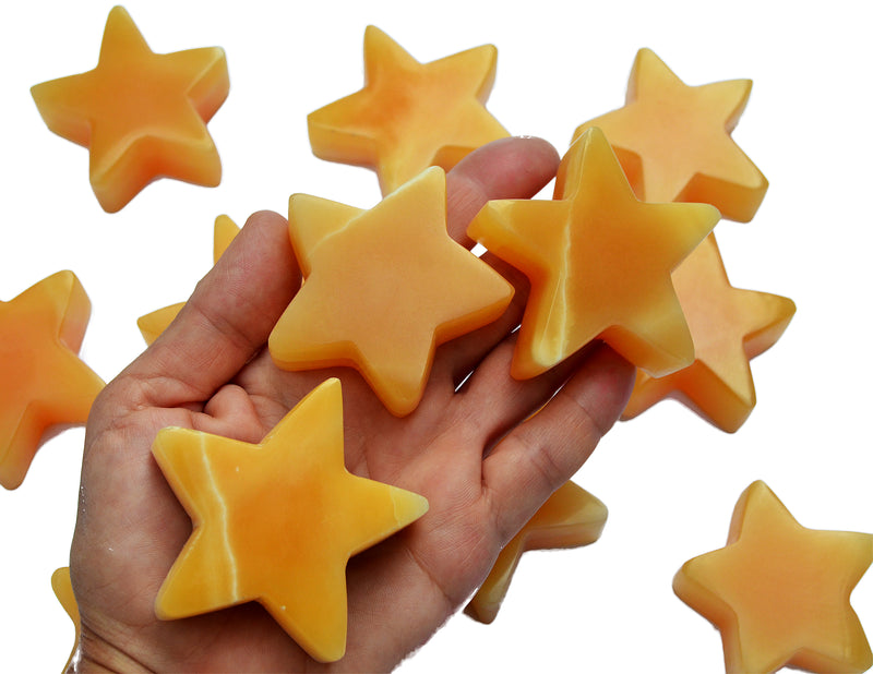 Three orange calcite star carving crystals 55mm-60mm on hand with background with some stones on white