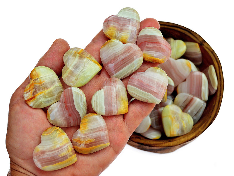 Ten pink banded onyx heart crystals 30mm on hand with background with some hearts inside a wood bowl