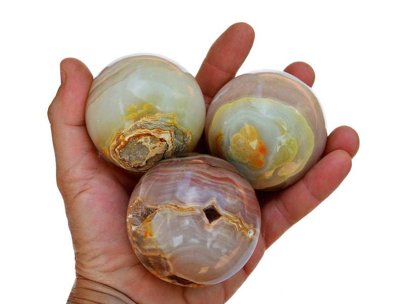 Three pink banded onyx spheres 50mm-60mm on hand with white background