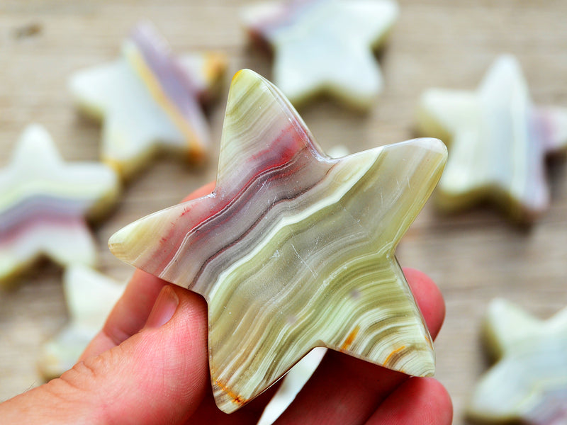 One pink banded onyx star carved crystal 55mm on hand with background with some gemstones on wood table