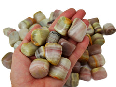 Some pink banded onyx tumbled crystals on hand with background with several stones on white