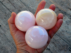 Three pink mangano calcite spheres 50mm-55mm on hand with wood background