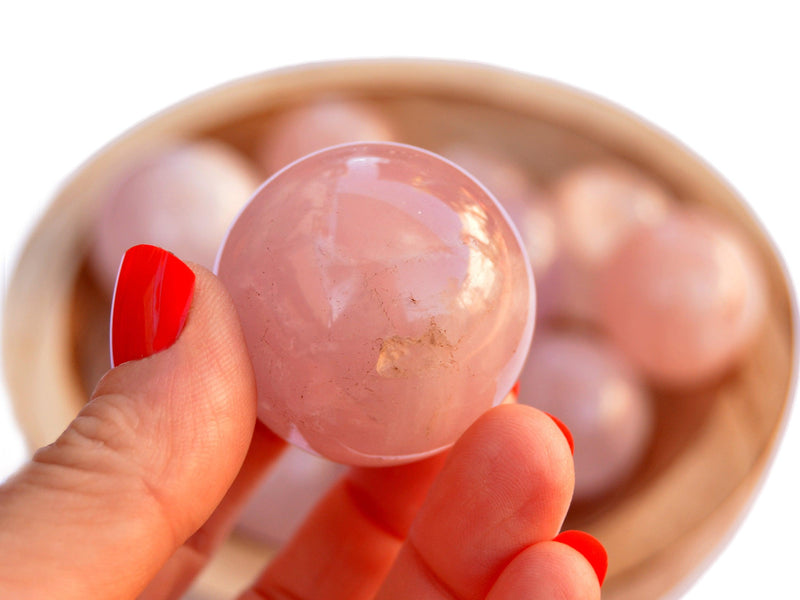 One rose quartz crystal sphere 30mm on hand with background with several crystals inside a wood bowl on white 