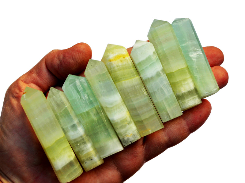 Hand holding a row of green pistachio calcite points against a white background