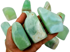 Three green pistachio calcite free forms 60mm-90mm on hand with background with some stones on white