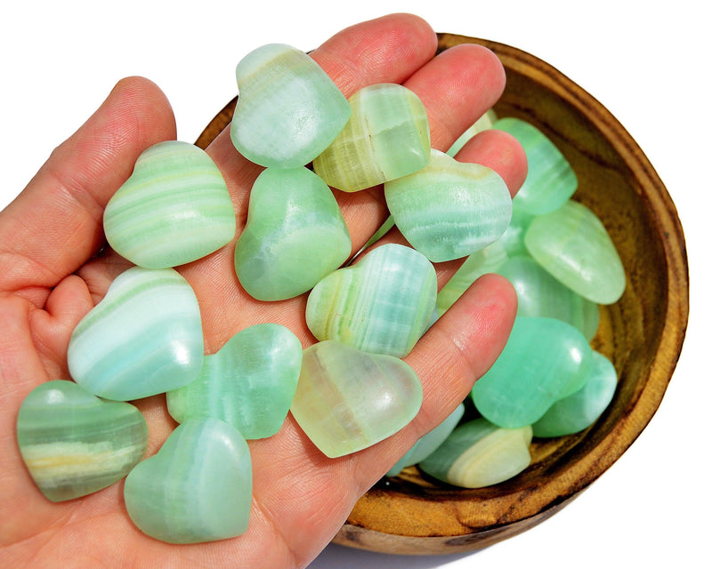 Ten green pistachio calcite crystal hearts 35mm-40mm on hand with background with some hearts inside a wood bowl on white