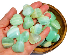 Ten green pistachio calcite crystal hearts 35mm-40mm on hand with background with some hearts inside a wood bowl on white