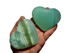 Two large pistachio calcite crystal hearts 70mm-80mm on hand with white background
