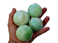 Four pistachio calcite spheres 40mm - 60mm on hand with white background