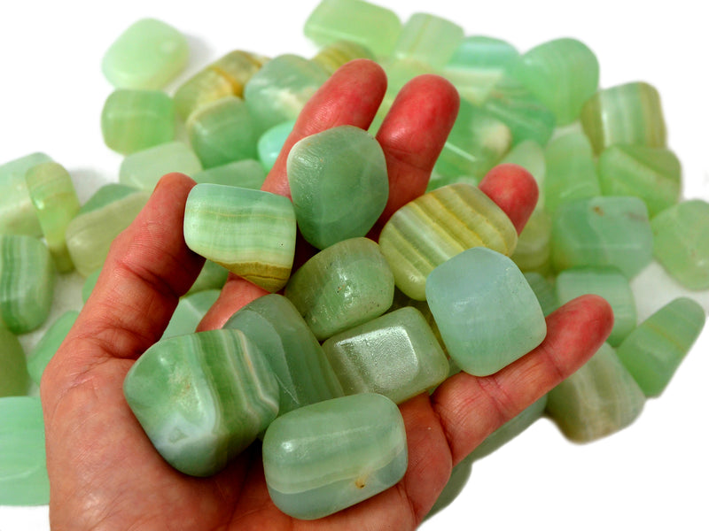 Some pistachio calcite cube tumbled stones on hand with background with several crystals on white