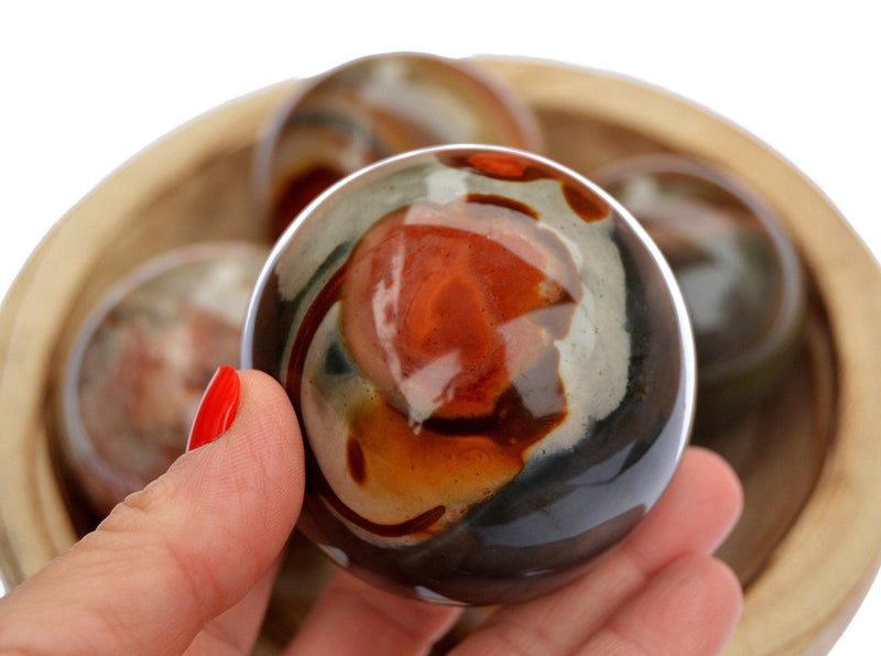 One polychrome jasper sphere 55mm on hand with background with some spheres inside a wood bowl