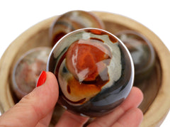 One polychrome jasper sphere 55mm on hand with background with some spheres inside a wood bowl