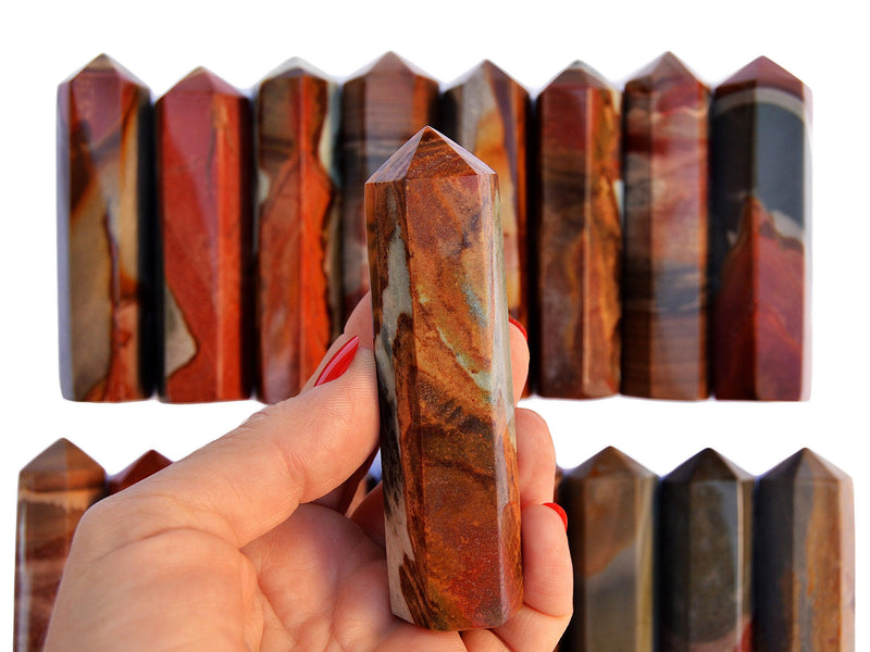 One desert jasper crystal obelisk 90mm on hand with background with some points on white