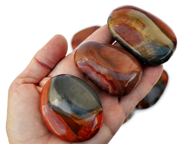 Three polychrome jasper palm stones 40mm - 70mm on hand with background with some crystals on white