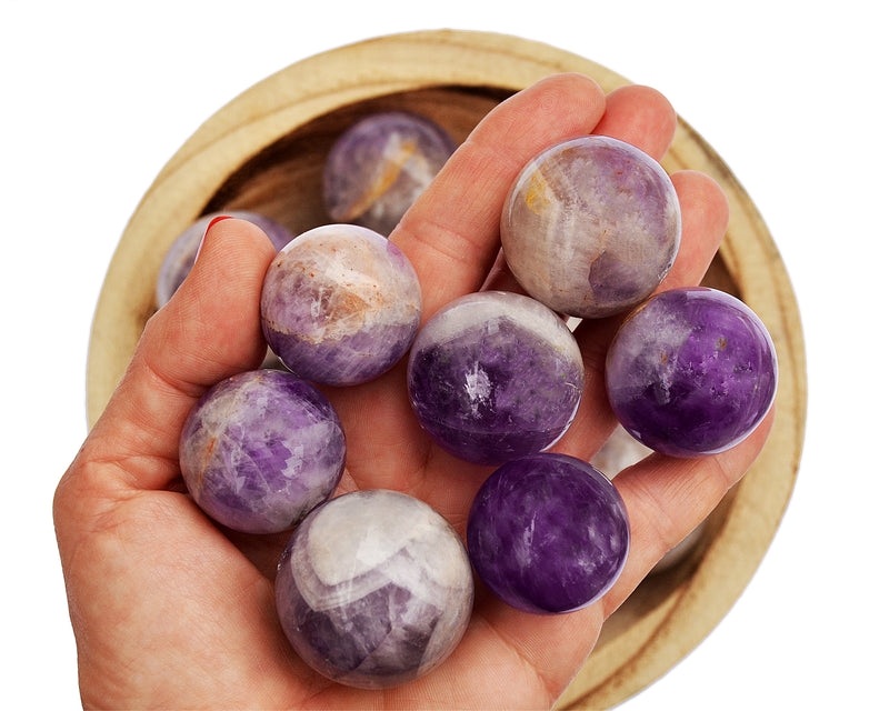 Several amethyst crystal balls 25mm - 50mm on hand with background with some stones inside a bowl