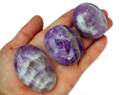 Three amethyst crystal palm stones 40mm - 60mm on hand with white background