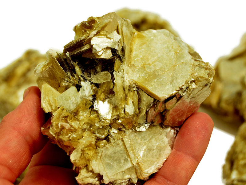 One raw muscovite crystal 100mm on hand with background with some stones on white