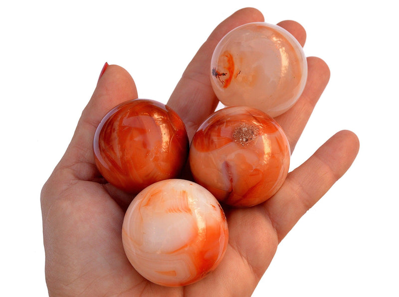 Four carnelian crystal spheres 45mm-50mm on hand with white background