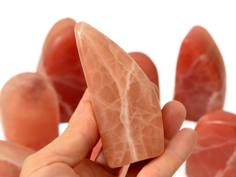 One rose calcite free form stone 70mm on hand with background with some crystals