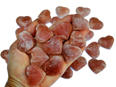 Ten rose calcite hearts 30mm-40mm on hand with background with some stones on white