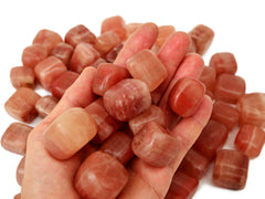 Some mini rose calcite tumbled on hand with background with several crystals on white 