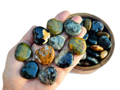 Ten ocean jasper heart crystals 30mm on hand with background with some hearts inside a wood bowl