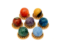 Mini spheres of polychrome jasper, carnelian, yellow septaria, chrysocolla, blue calcite, blue apatite and amethyst stones forming a circle on wooden bases on a white background.