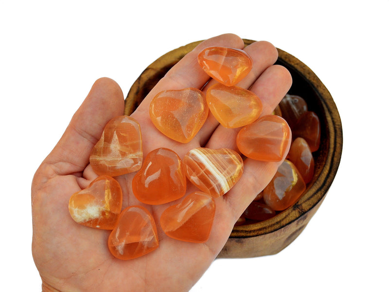 Ten honey calcite crystal hearts small 25mm-30mm on hand with background with some hearts inside a bowl on white