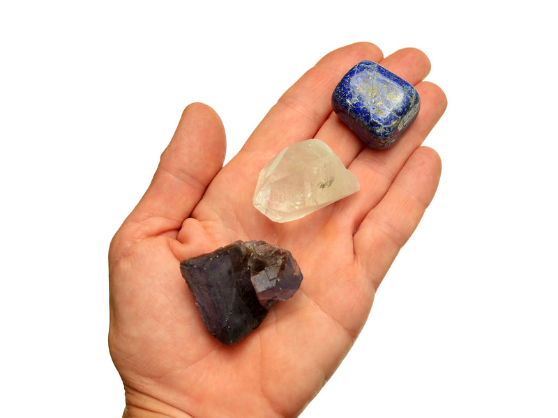 One raw cubic purple fluorite, clear quartz point and lapis lazuli tumbled 30mm-40mm on hand with white background