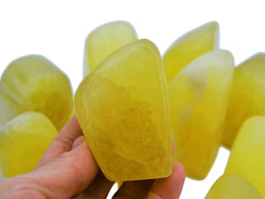 One yellow calcite free form stone on hand with background with some stones on white